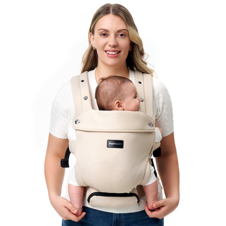 Translation missing: en.Momcozy baby carrier in beige, worn by a smiling woman, securely holding an infant. Ergonomic design for comfort and support